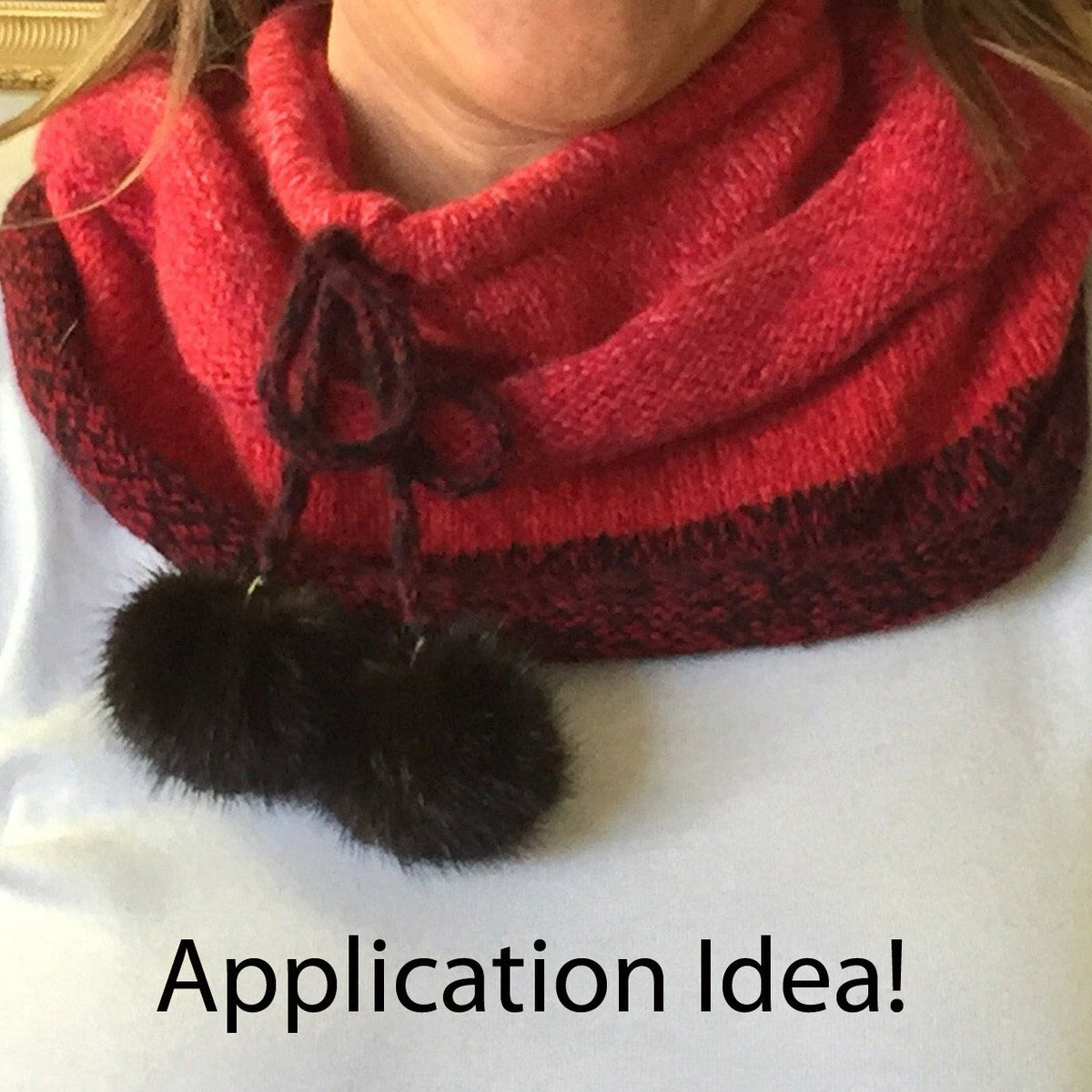 A close-up of a person wearing a red and black knit cowl scarf with two mink-fur pom-poms hanging from the front. The person is wearing a white long-sleeve top, and the text 'Application Idea!' is overlaid at the bottom.
