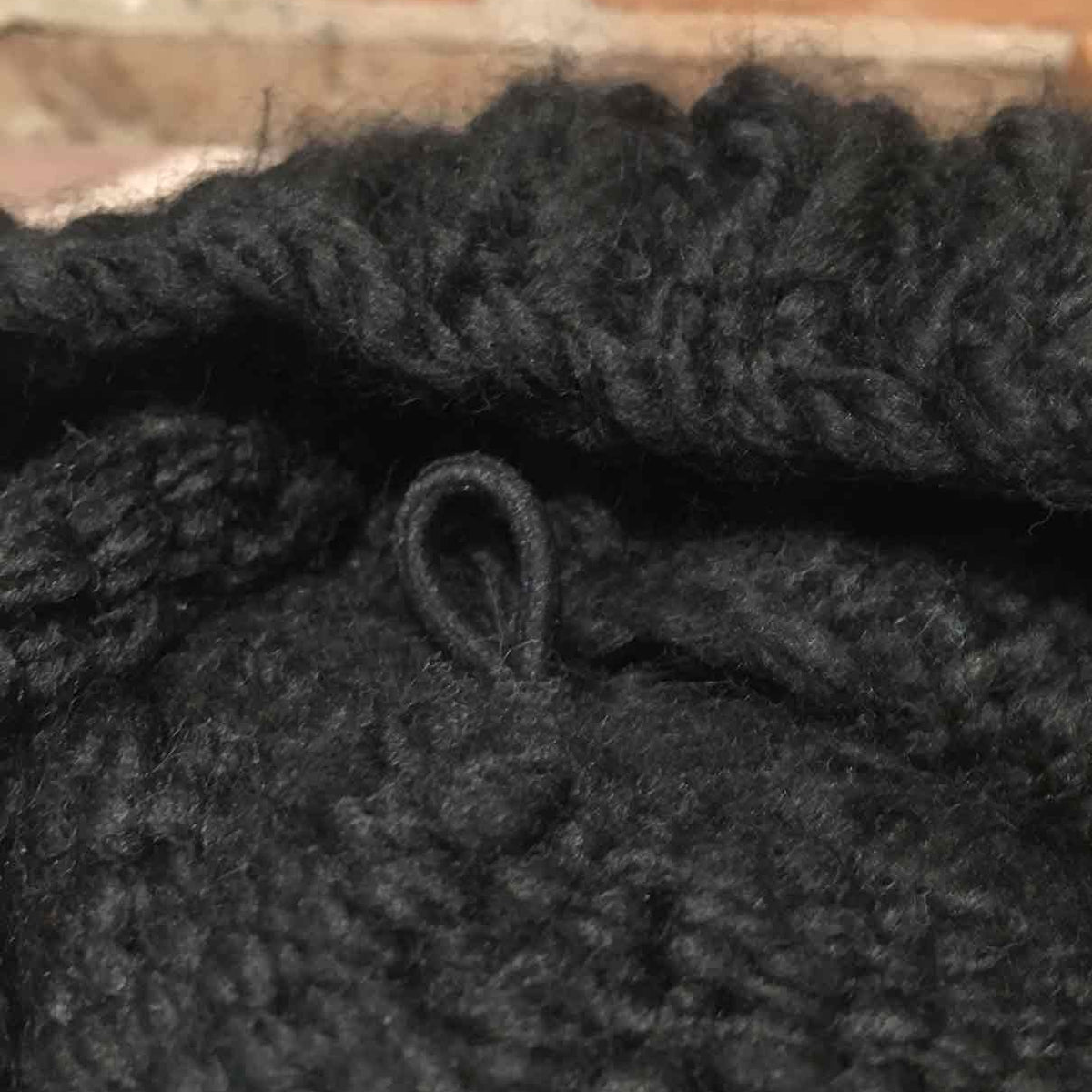 Close-up of a black chunky knit fabric with a small black loop detail, showing the thick yarn texture.