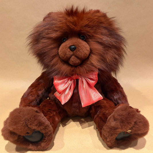 A brown plush teddy bear with a shaggy lion-like mane, wearing a shiny pink bow tie, sitting against a plain beige background.