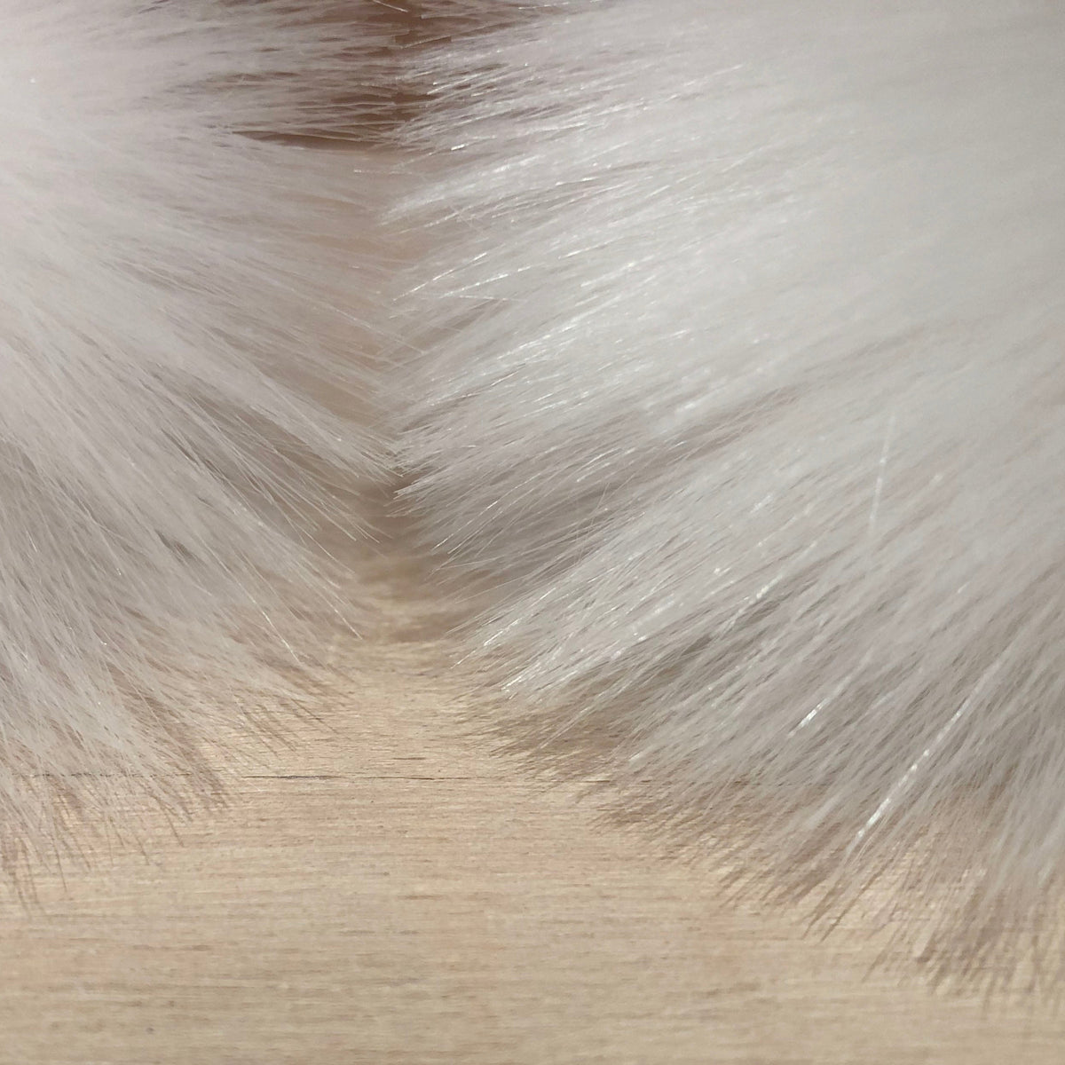 A close-up of white faux fur trim with soft, fluffy fibers framing a light beige wood surface.