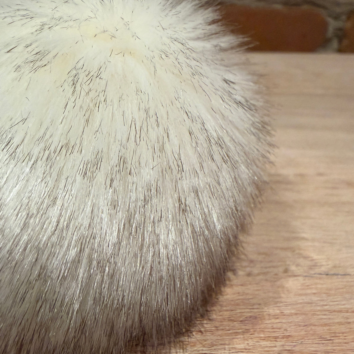 Close-up of a fluffy cream-colored faux fur or sheepskin material with dark brown tips, resting on a light wood surface.