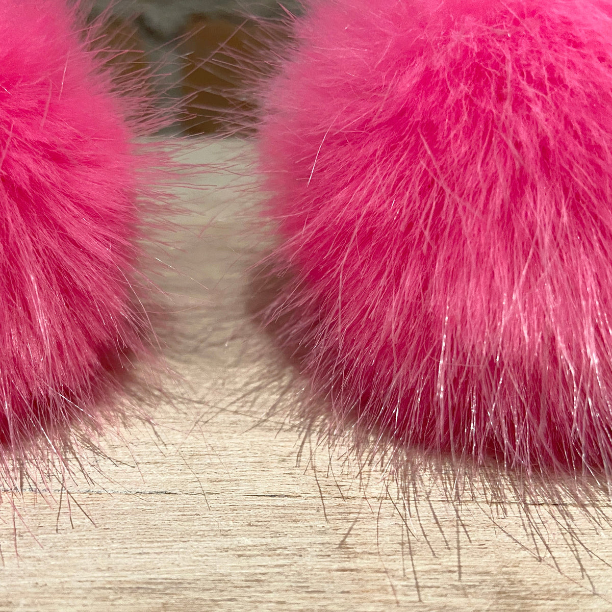 A close-up of a pair of fluffy bright pink pom poms on a light wood floor.