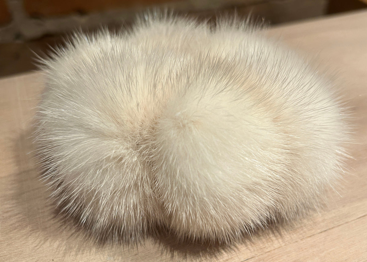A fluffy mink fur scrunchie, photographed on a light wood surface with a blurred brick wall in the background.