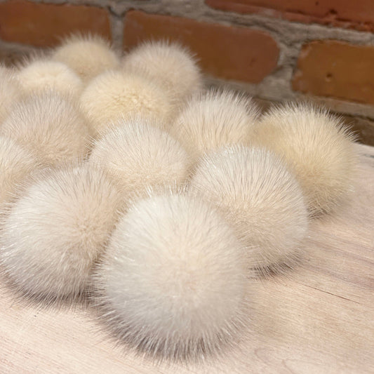 A group of fluffy cream-colored pom-poms arranged on a light wood surface with a brick wall in the background.