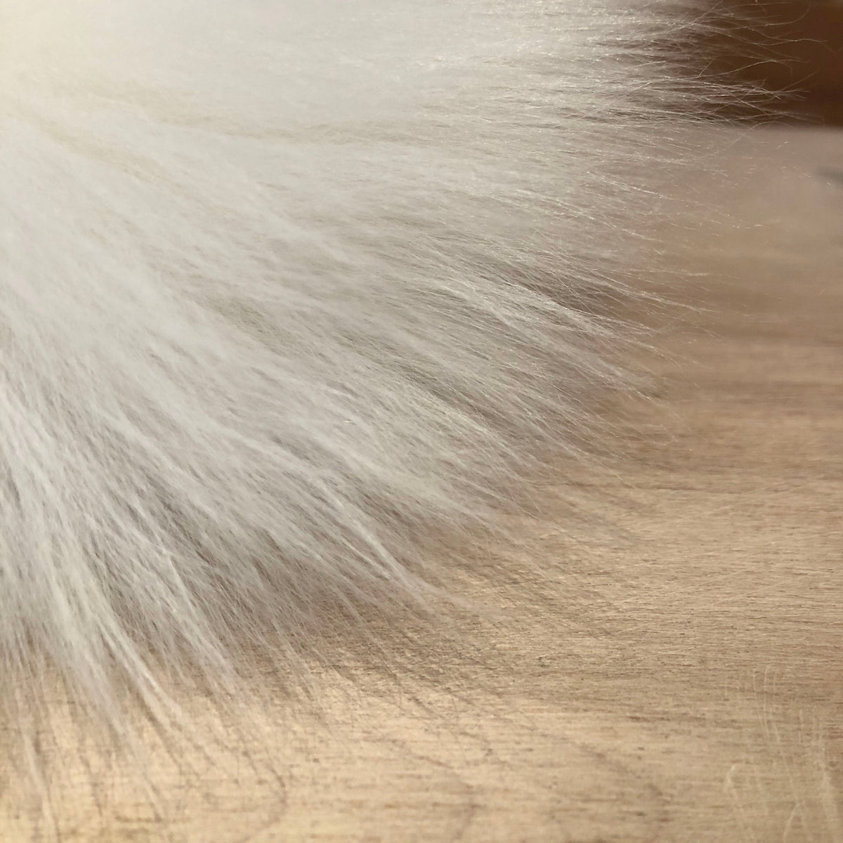 A close-up of fluffy white lamb fur or a white fur trim resting on a light wood surface.