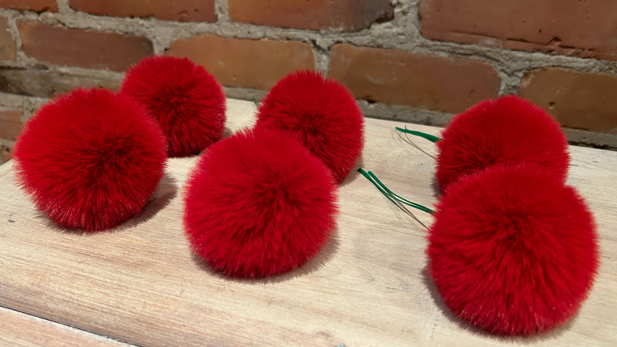Five bright red fluffy pom-pom christmas tree ornaments arranged on a light wood surface with a brick wall background.