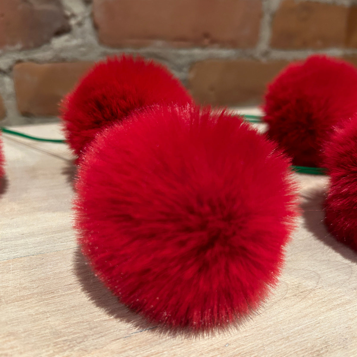 Bright red fluffy pom-pom christmas tree ornaments on a wooden surface with a brick wall background.