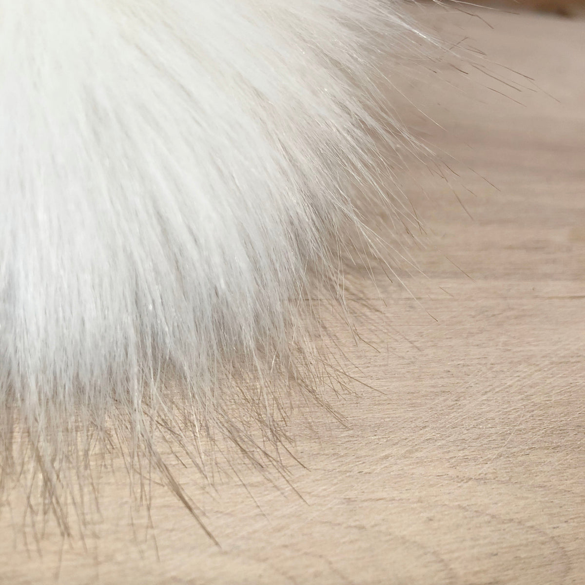 A close-up of a fluffy white faux fur trim or accessory resting on a light beige textured surface.