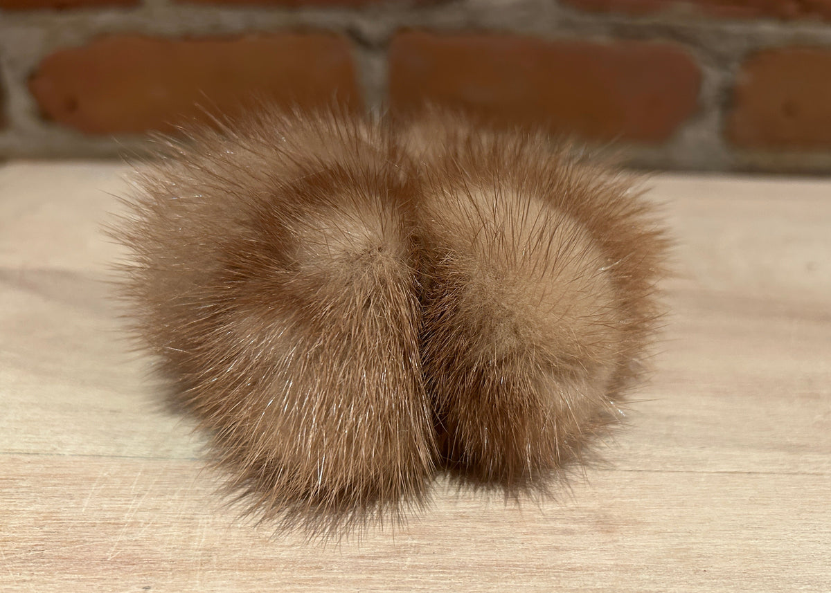 A gold mink scrunchie resting on a light wood surface with a blurred brick wall background.