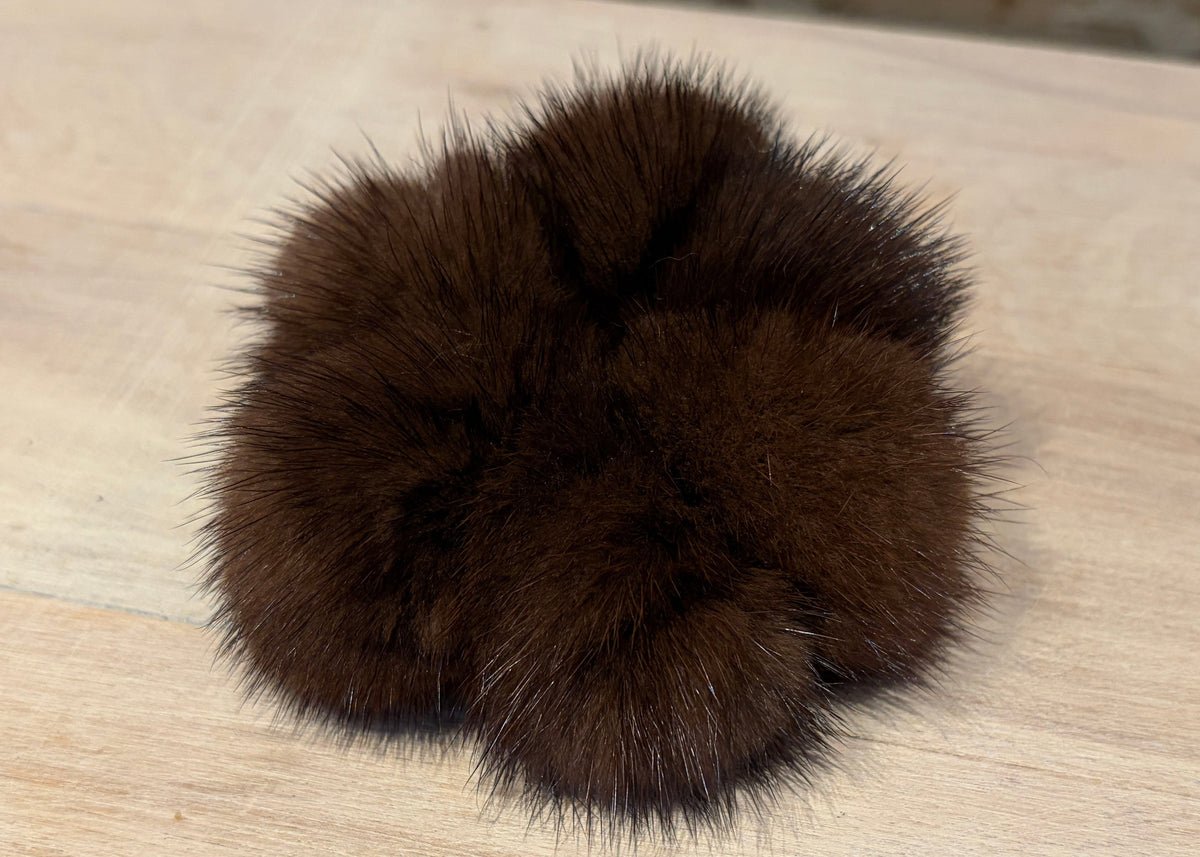 A dark brown fluffy mink fur pom-pom accessory resting on a light wood surface.