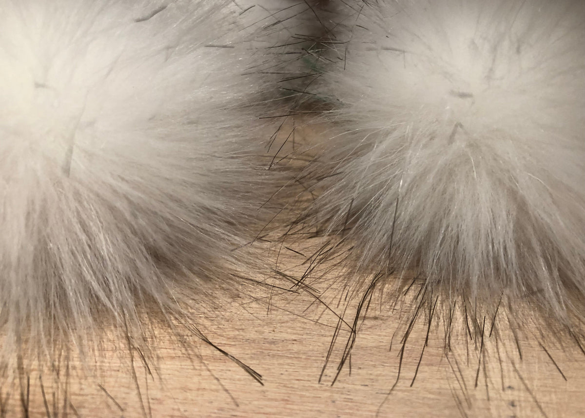 A white faux fur pom-pom christmas tree ornament, resting on a light wood tabletop.