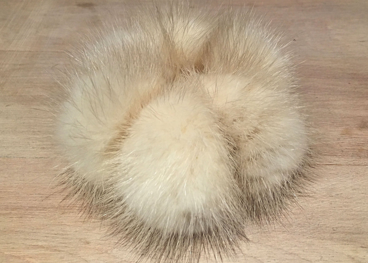 A cluster of fluffy mink fur pom-poms in a light cream or beige color, resting on a light wood surface.