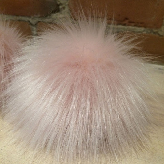 A close-up of a fluffy light pink faux fur pom-pom against a neutral background.