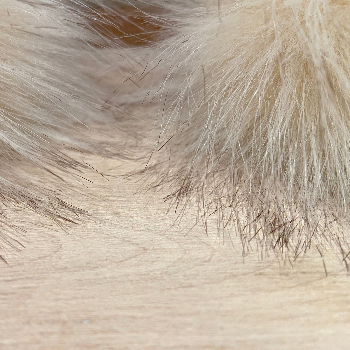 Close-up of a light beige faux fur or sheepskin material with fine fibers resting on a pale wood surface.