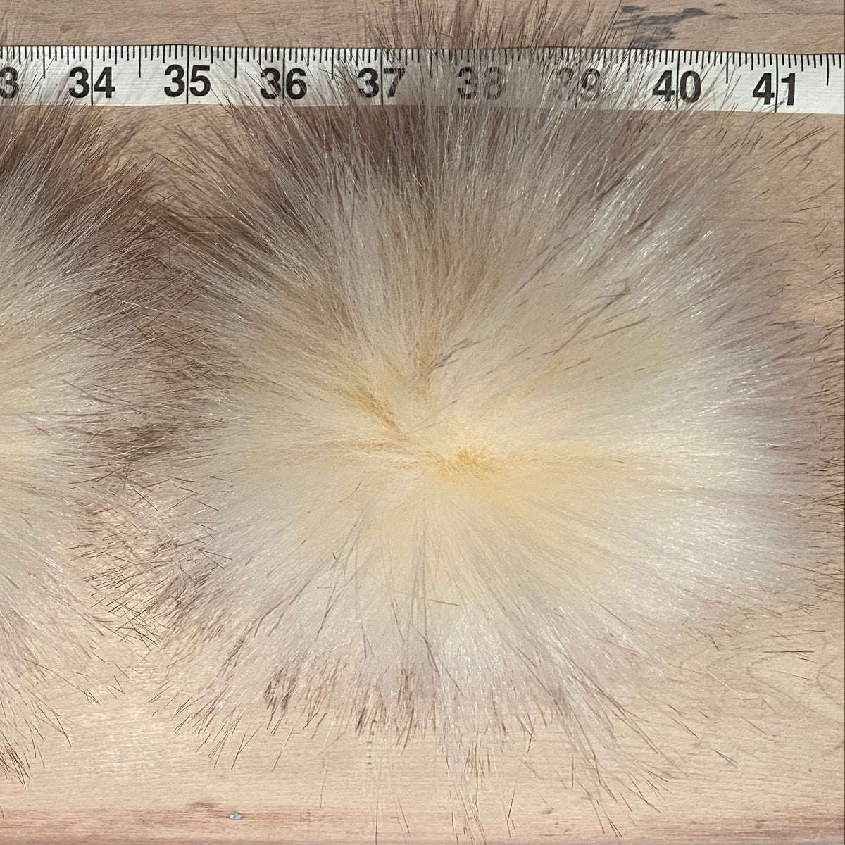 A close-up of fluffy faux fur or a fur-like textile sample spread out on a light wood surface, with a measuring ruler along the top edge to show scale.