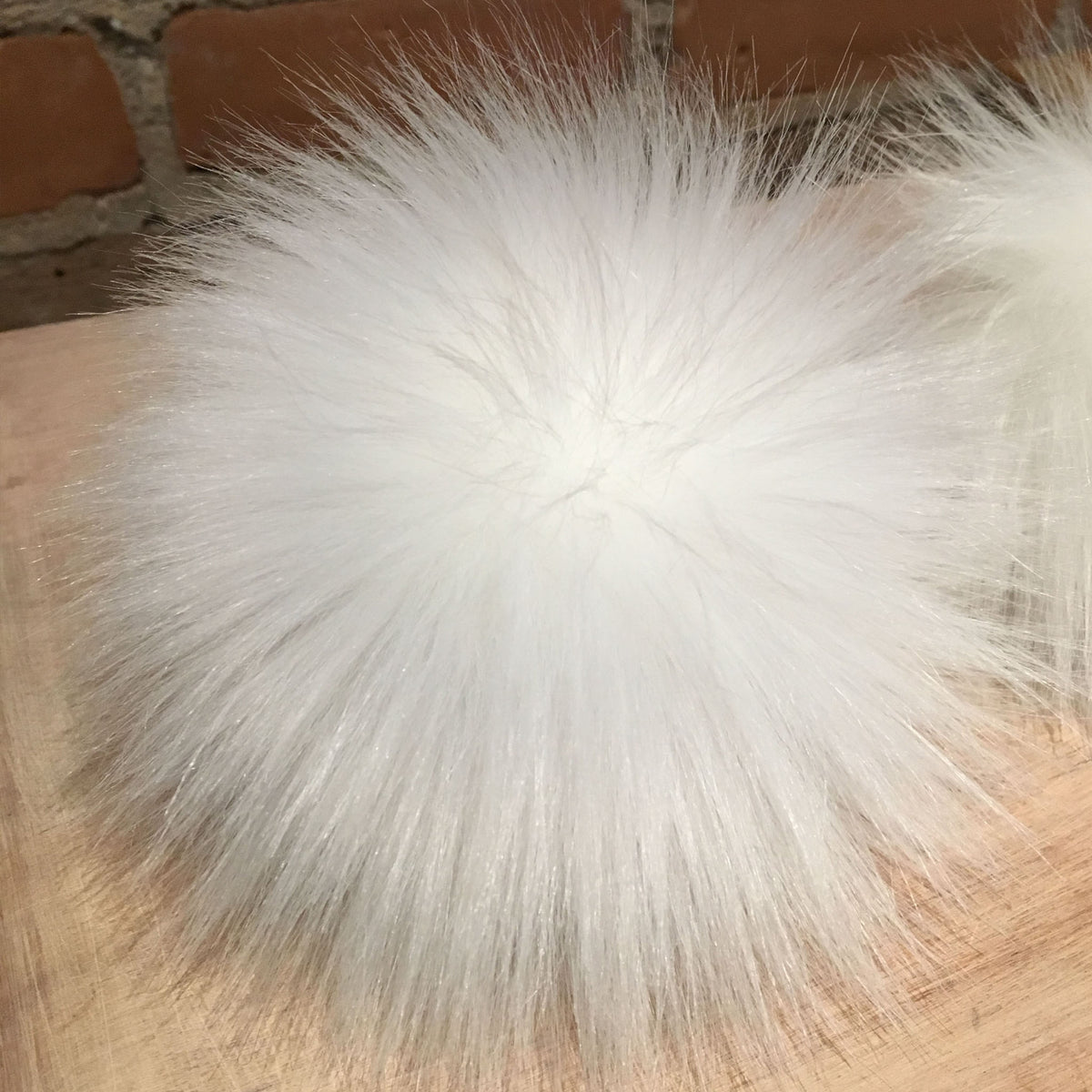 A large bright white faux lamb fur pom pom on a wooden surface.